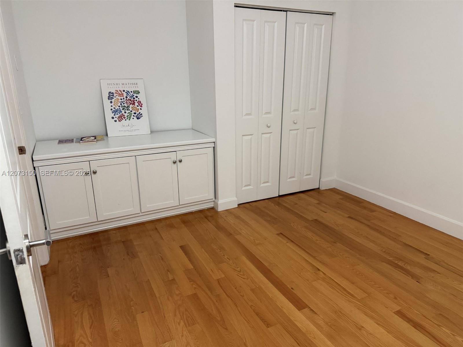 Wood-finish flooring, built-in white cabinetry with countertop, and bi-fold closet doors