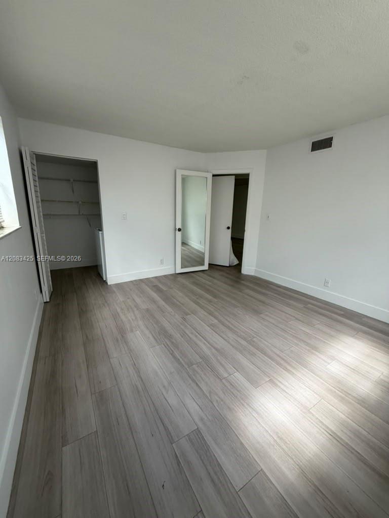 Room featuring wood-finish flooring, a walk-in closet with built-in shelving, and a door with a full-length integrated mirror