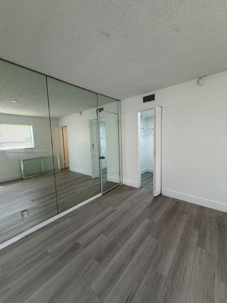 Wood-finish flooring, full-wall mirrored paneling, and closet with louvered door Wood-finish flooring, full-wall mirrored paneling, and closet with louvered door