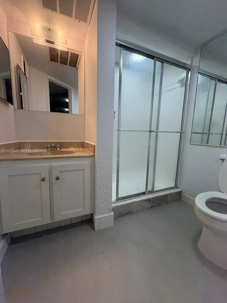 Bathroom featuring a vanity with white cabinetry, a neutral countertop with an integrated basin, a walk-in shower with sliding glass doors, and wall-mounted mirrors