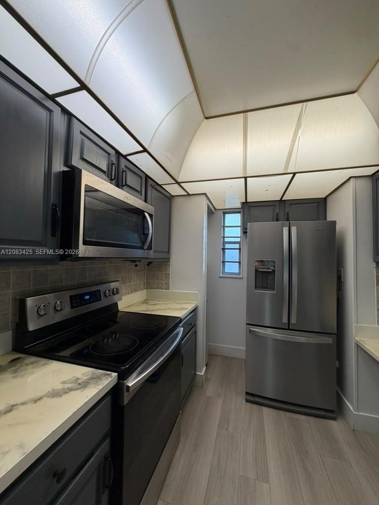Kitchen featuring dark-toned cabinetry, light-toned countertops with a marble-patterned finish, wood-finish flooring, and stainless steel appliances Kitchen featuring dark-toned cabinetry, light-toned countertops with a marble-patterned finish, wood-finish flooring, and stainless steel appliances