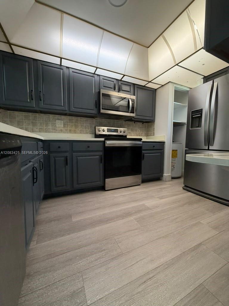 Kitchen featuring dark-toned cabinetry, stainless steel appliances, wood-finish flooring, and a coffered ceiling with inset lighting Kitchen featuring dark-toned cabinetry, stainless steel appliances, wood-finish flooring, and a coffered ceiling with inset lighting