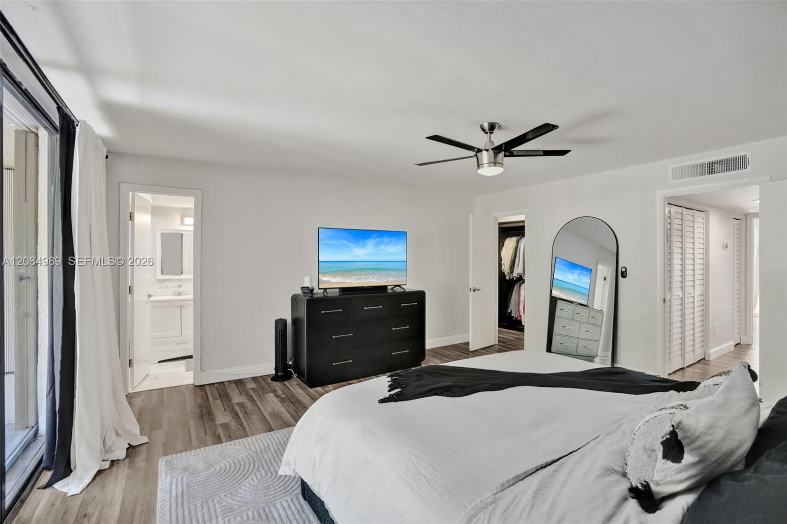 Neutral-toned wood-finish flooring, brushed metal ceiling fan, and louvered closet doors