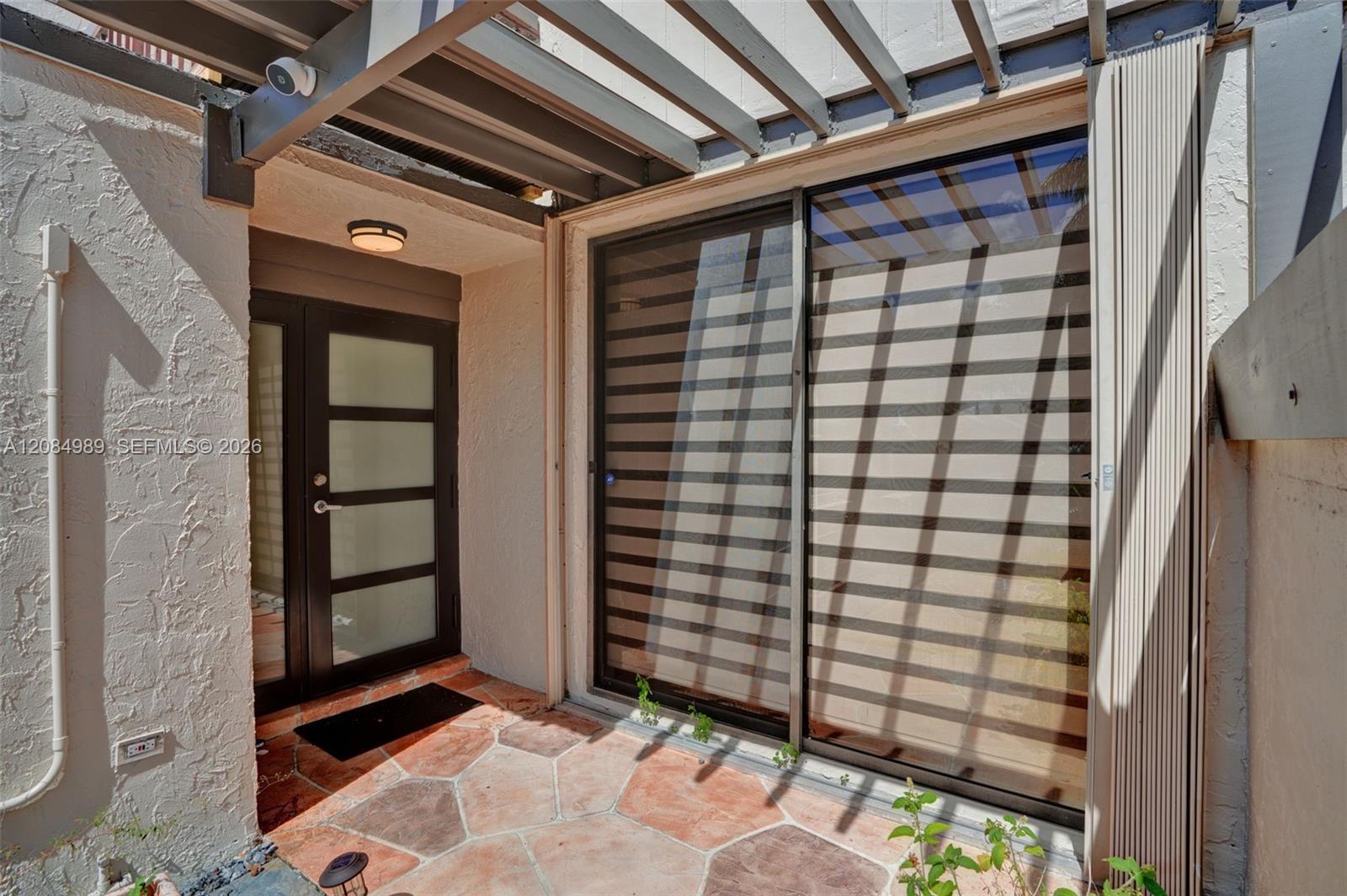 Private patio featuring natural stone pavers, a fixed wooden pergola, multi-panel glass sliding door, and a frosted glass-panel entry door