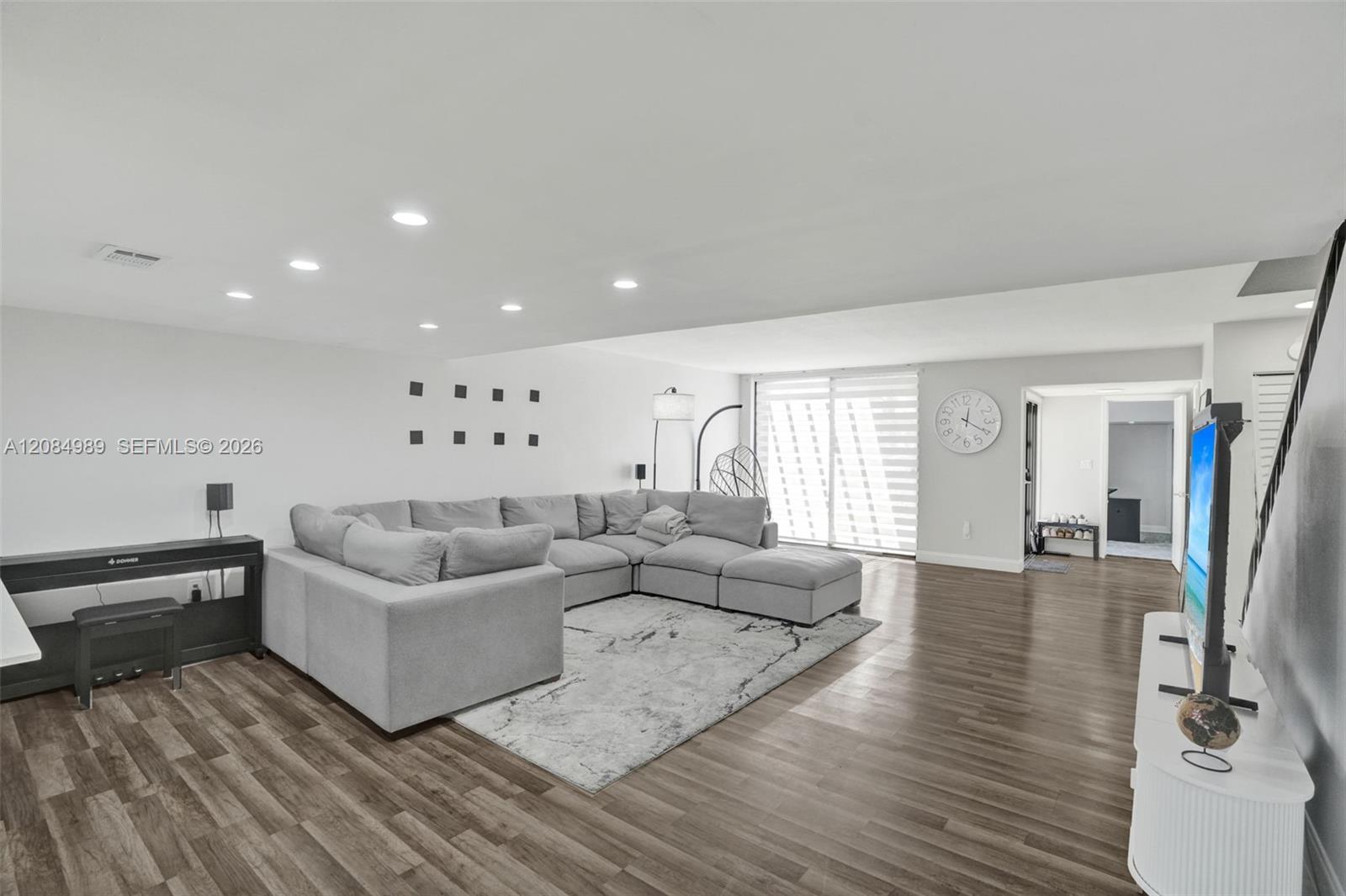 Open-concept interior featuring wood-finish flooring, recessed lighting, and a large sliding glass door with horizontal blinds