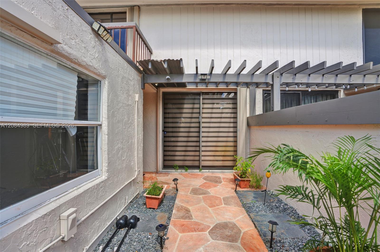 Private courtyard featuring a stone paver walkway, decorative pergola, stone-textured exterior walls, sliding glass door, and a second-story balcony with railing