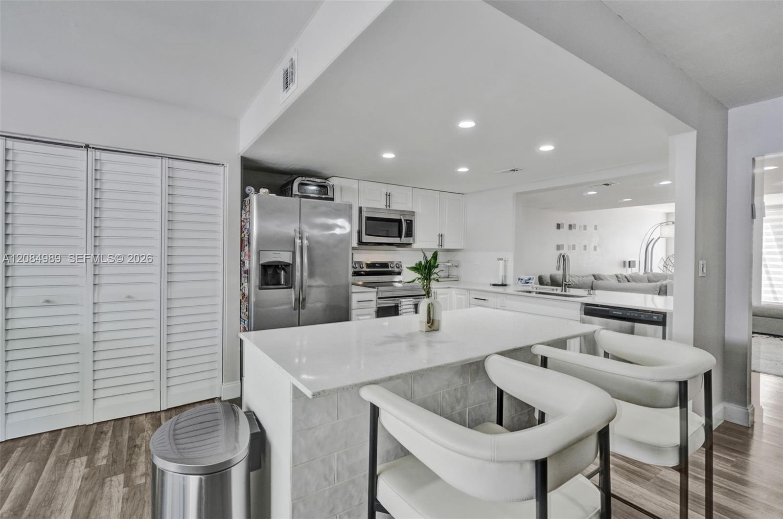 Kitchen featuring a stone-surface island, stainless steel appliances, white cabinetry, recessed lighting, and wood-finish flooring