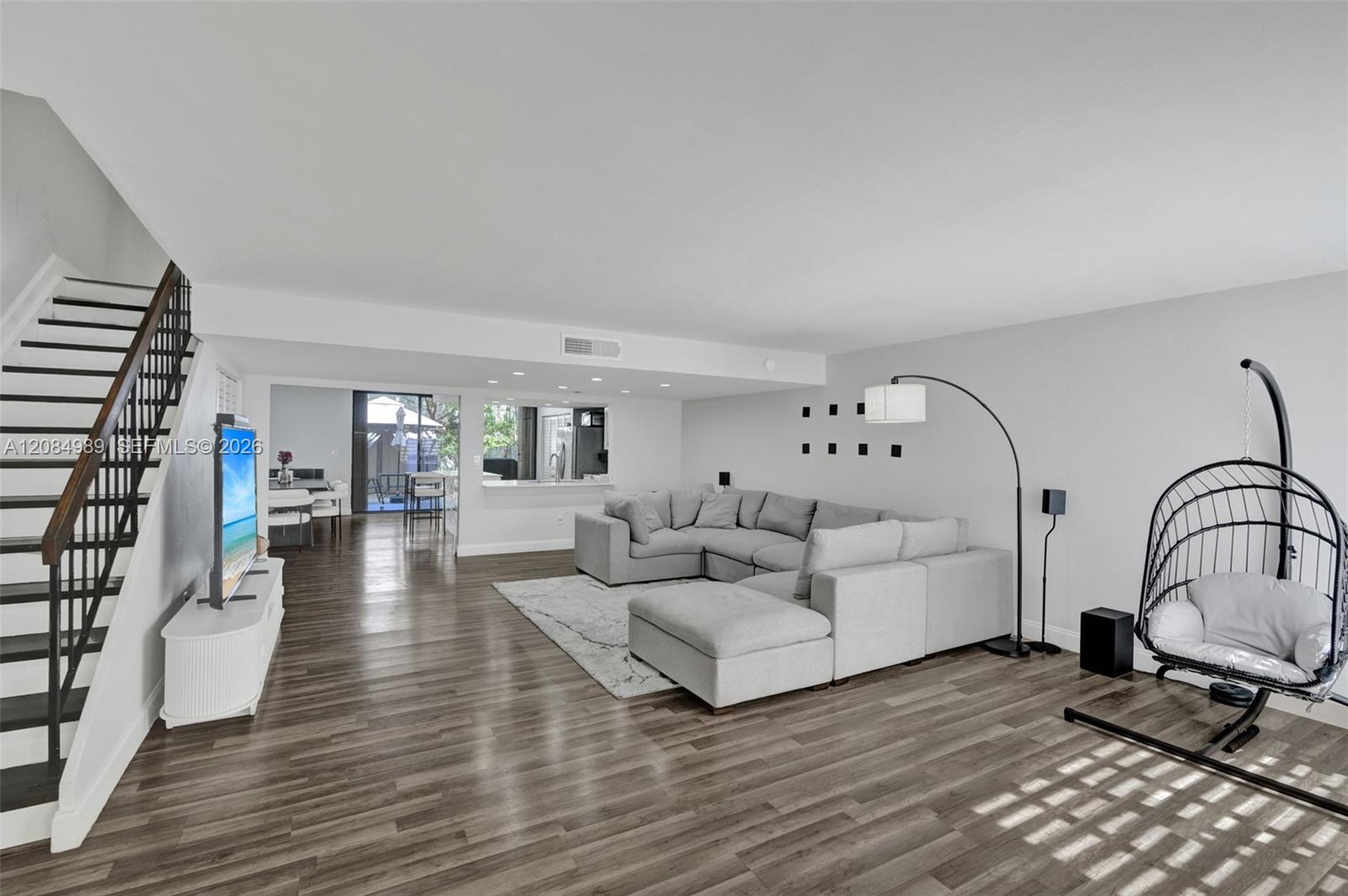 Open-concept living space featuring wood-finish flooring, recessed lighting, and a staircase with a metal railing and wood handrail