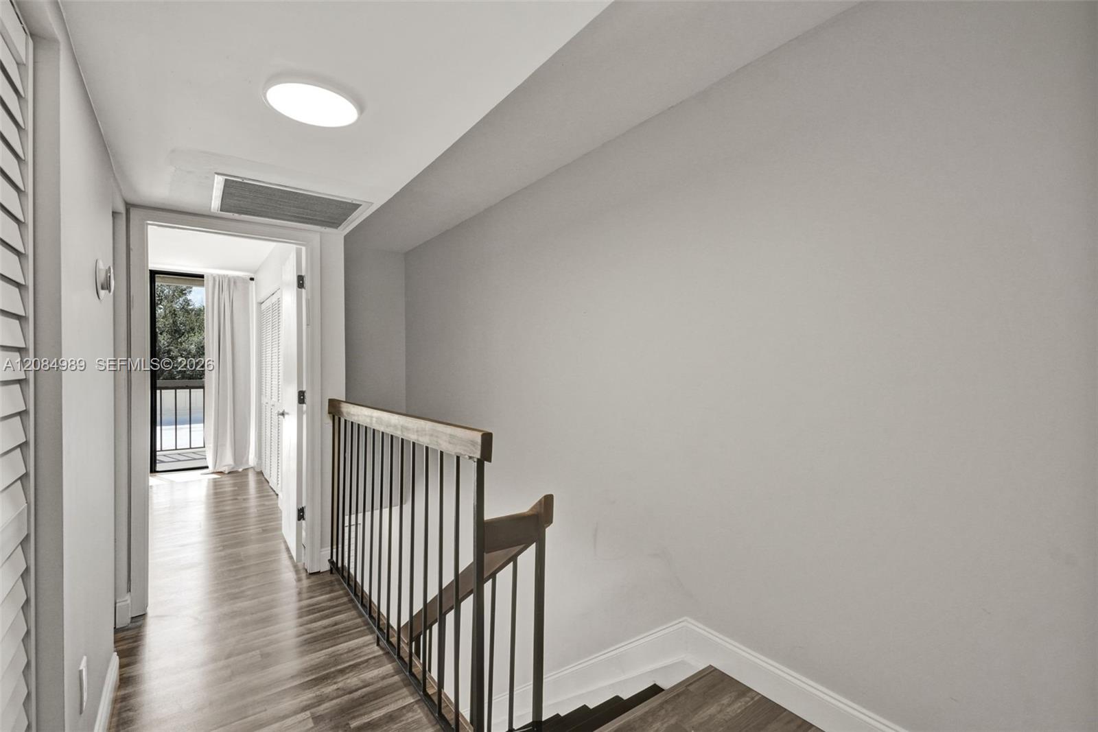 Wood-finish flooring, staircase featuring a dark-toned handrail, and metal balusters