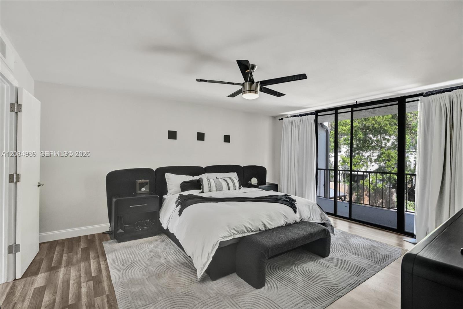 Room featuring wood-finish flooring, a matte black multi-blade ceiling fan with integrated lighting, and floor-to-ceiling sliding glass doors opening to a private balcony