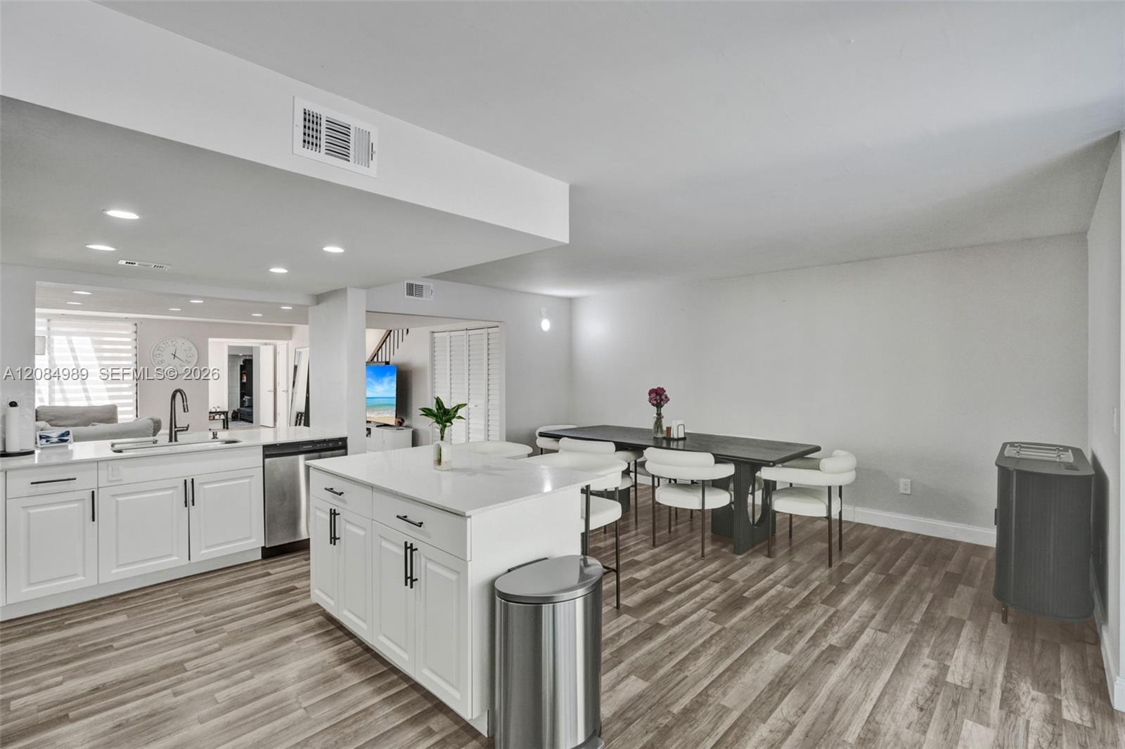 Kitchen featuring a central island with a solid surface countertop, white shaker-style cabinetry, stainless steel dishwasher, undermount sink with a gooseneck faucet, and wood-finish flooring