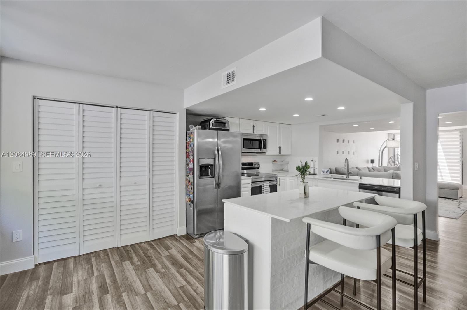 Kitchen featuring an island with a stone-finish countertop, stainless steel appliances, white cabinetry, louvered closet doors, and wood-finish flooring