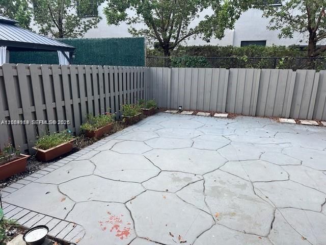 Private rear patio featuring a flagstone-patterned concrete surface, enclosed by a solid privacy fence with perimeter landscape planters