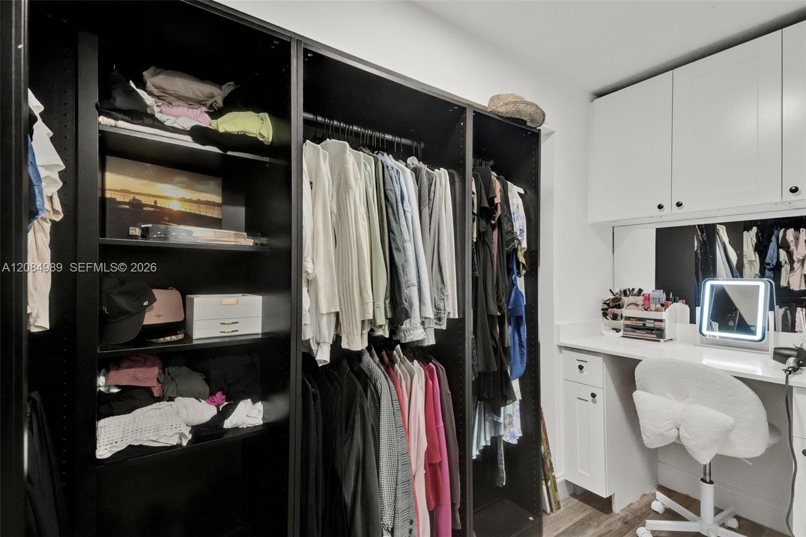 Custom dressing area featuring black built-in shelving, white overhead cabinetry, an integrated vanity with a stone countertop, and a wall-mounted mirror