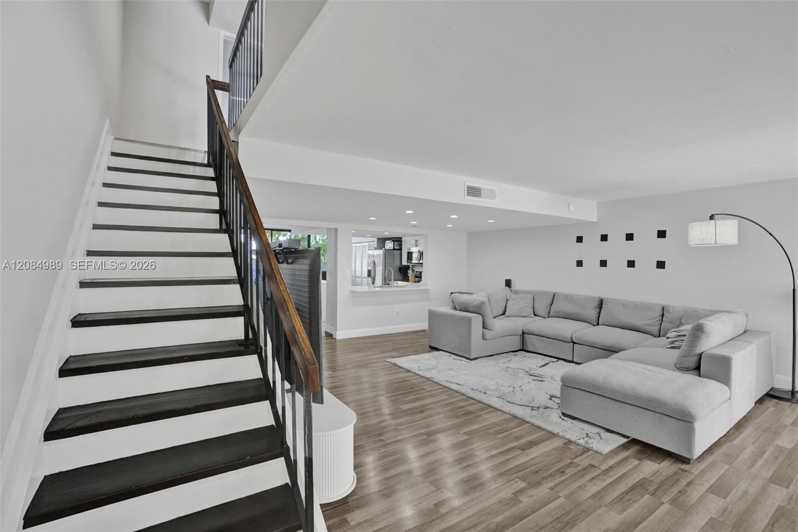 Staircase featuring dark-stained treads and a wrought-iron railing, wood-finish flooring, recessed lighting, and a service pass-through window with a quartz-style ledge