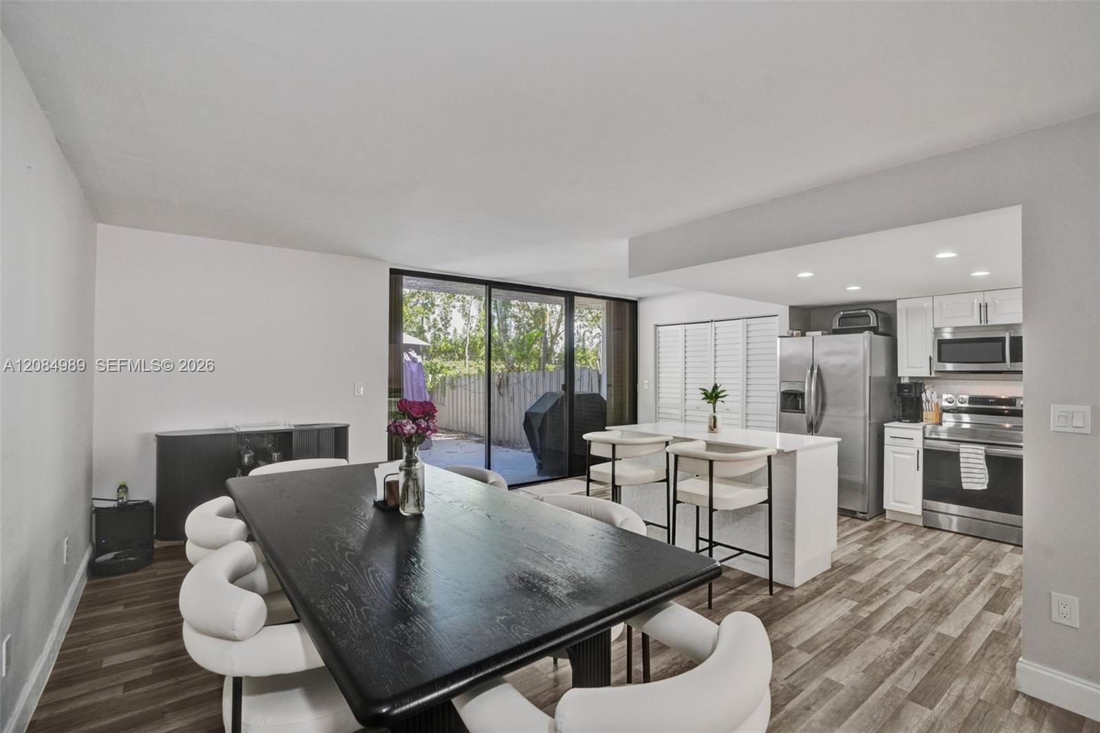 Open-concept kitchen and dining area featuring wood-finish flooring, a central island with countertop seating, stainless steel appliances, recessed lighting, and a large sliding glass door