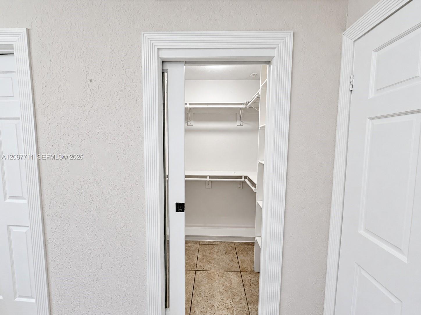 Walk-in closet featuring a sliding door, tiered white shelving, and tiled flooring