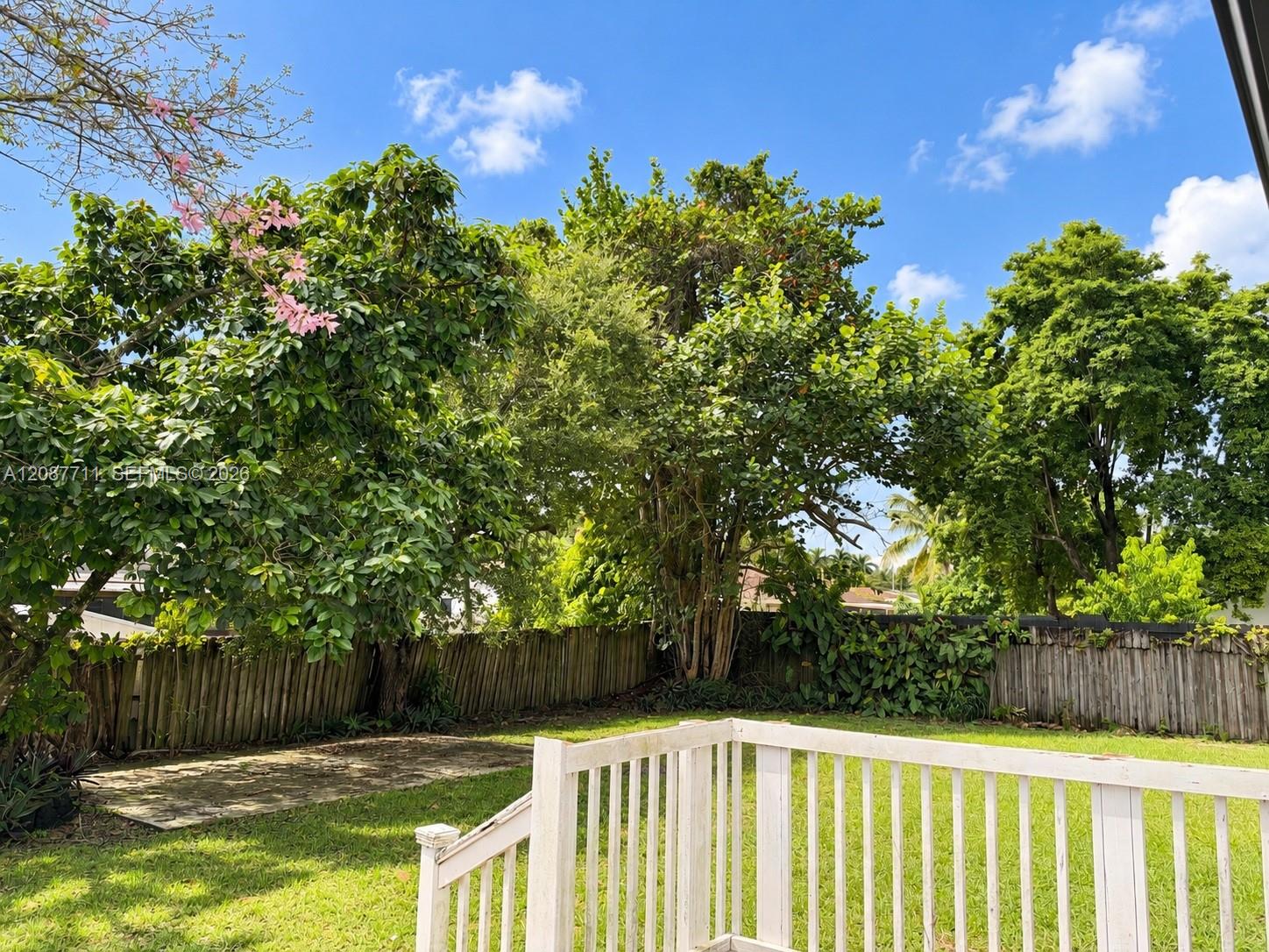 Backyard featuring a wood deck with white railings, a concrete patio, perimeter wood fencing, and mature trees