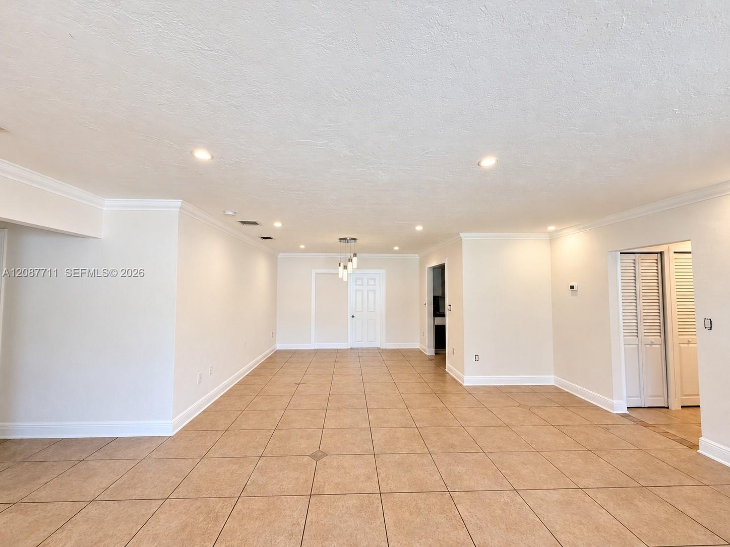 Open-concept interior featuring oversized tile flooring, recessed lighting, crown molding, and louvered closet doors