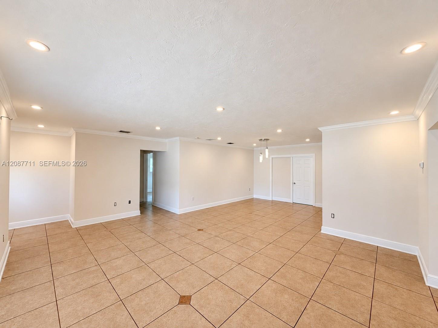Open-concept room featuring large-format ceramic tile flooring with decorative inserts, recessed lighting, crown molding, and a multi-pendant light fixture