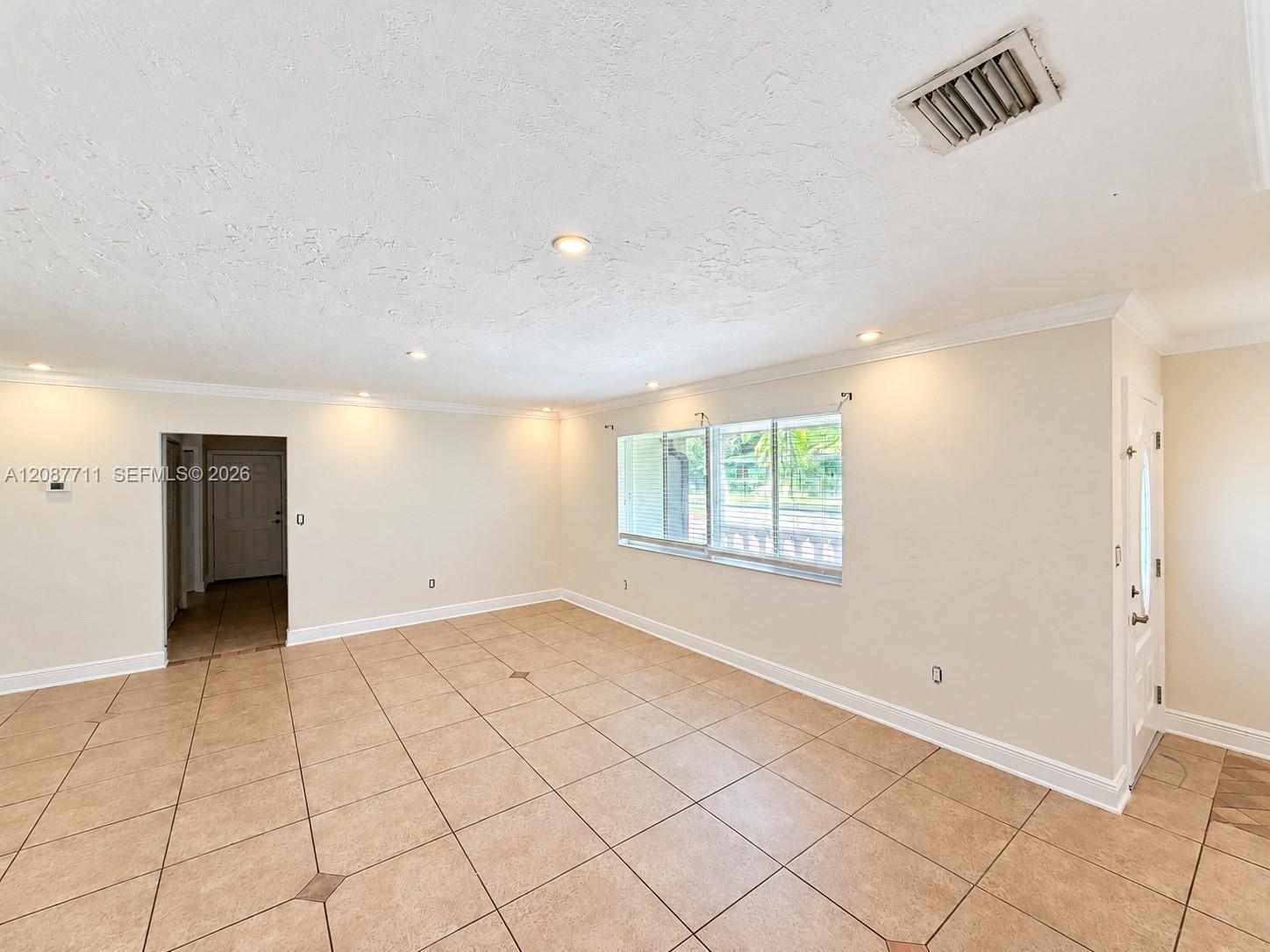 Neutral-toned tile flooring with decorative inserts, recessed lighting, crown molding, and large windows