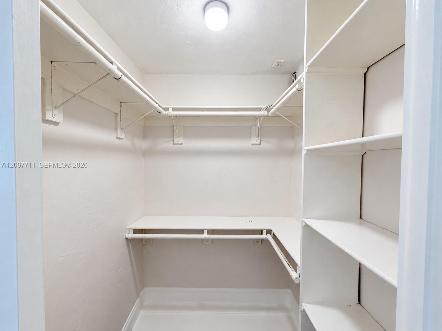 Walk-in closet featuring tiered wrap-around metal garment rods and custom built-in white shelving