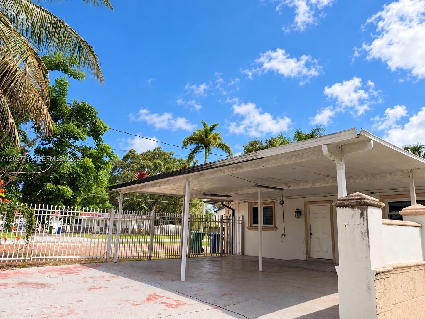 Covered concrete carport with integrated support pillars, gated perimeter fencing, and concrete driveway surface