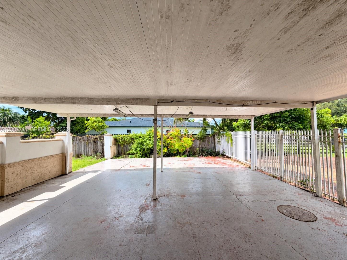 Covered parking area featuring a concrete floor, structural metal support posts, and a white aluminum privacy fence