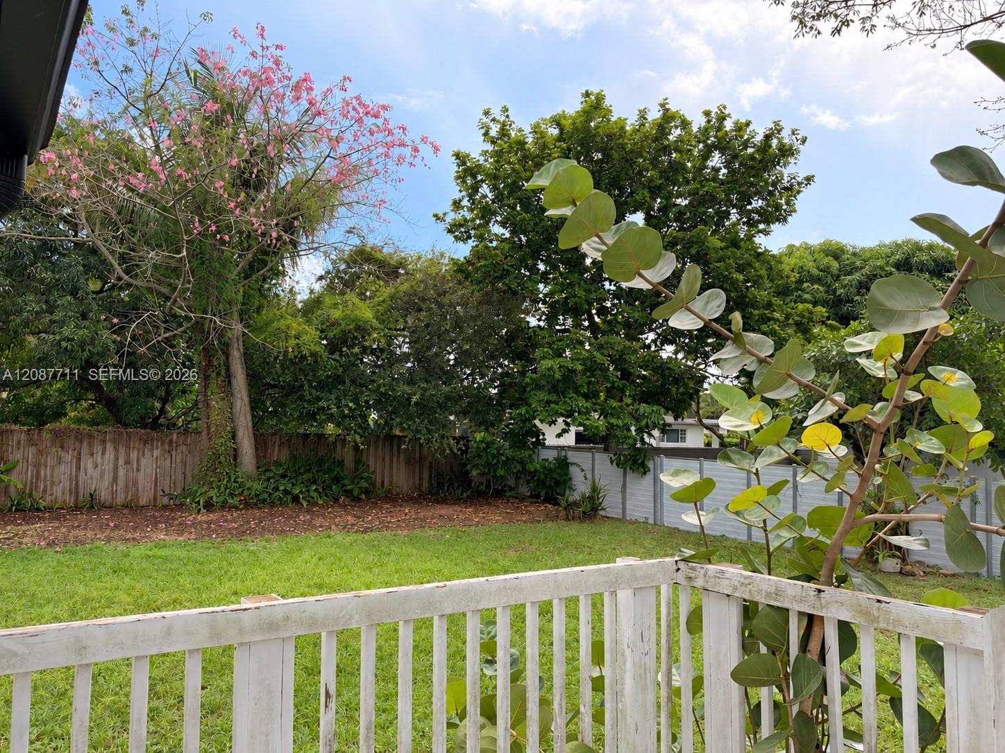 Rear yard featuring a grass lawn, perimeter wood fencing, and mature trees