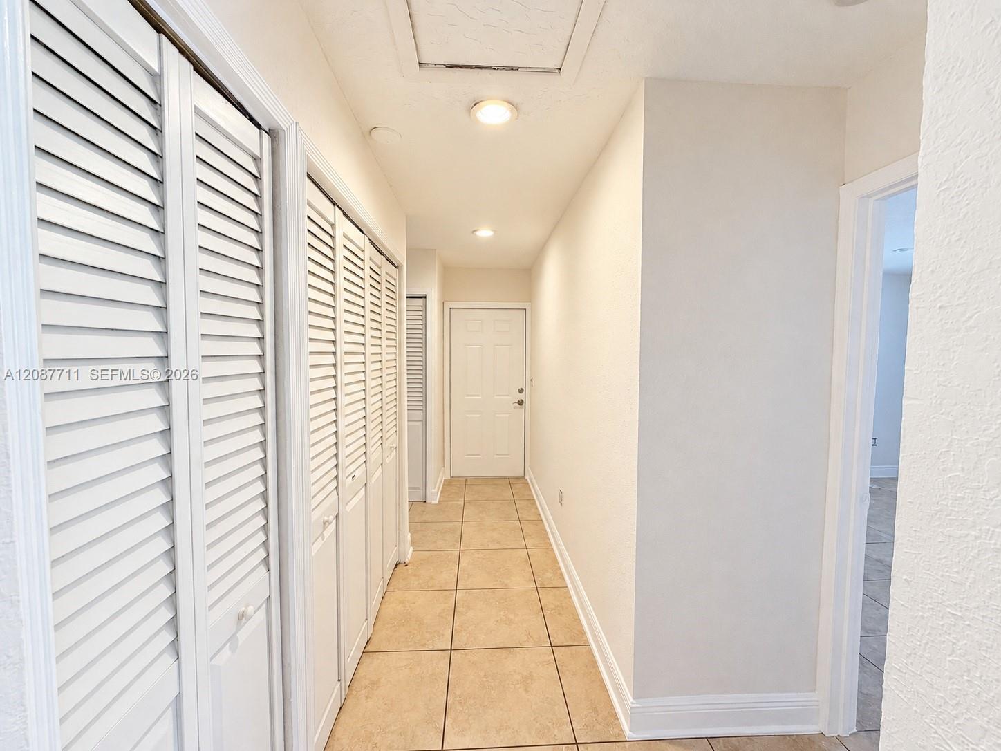 Hallway featuring ceramic tile flooring, multiple white louvered closet doors, and recessed lighting