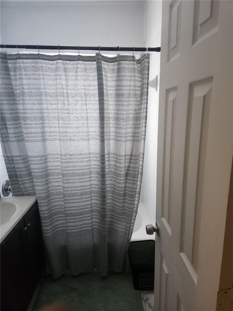 Bathroom featuring a vanity with a light-colored countertop and dark cabinetry, a shower-tub combination, and a six-panel interior door