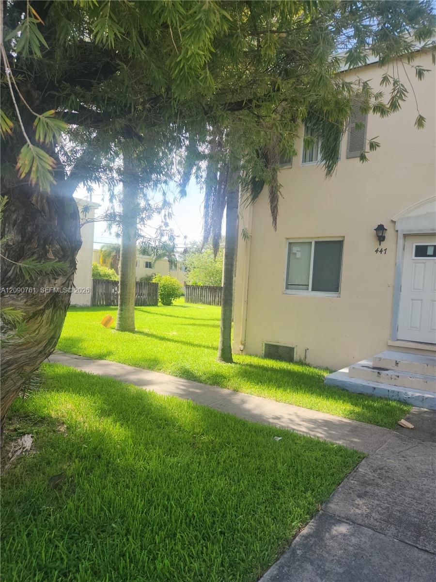Exterior elevation featuring a stucco facade, concrete walkway, mature trees, and an enclosed grass yard Exterior elevation featuring a stucco facade, concrete walkway, mature trees, and an enclosed grass yard