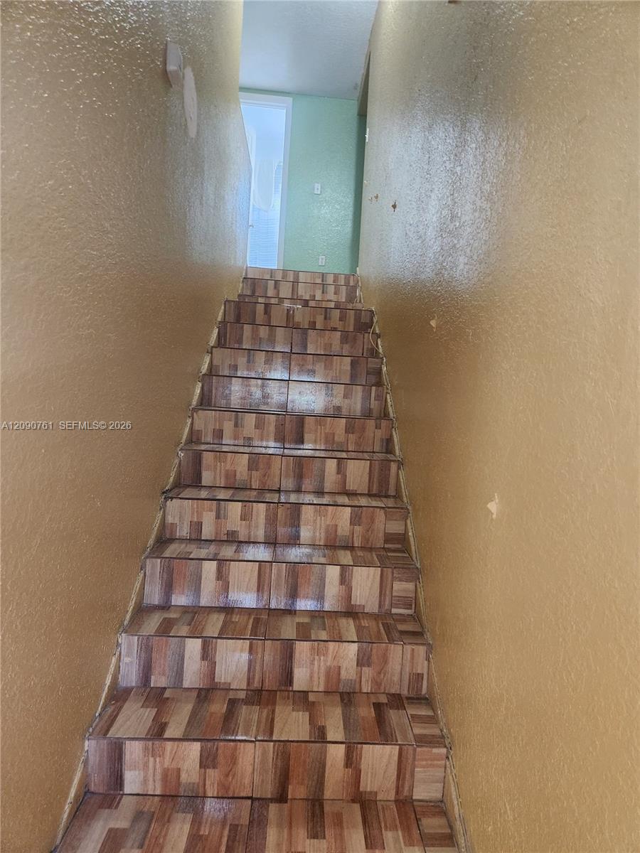 Staircase featuring tiled treads and risers with a multi-toned, wood-finish pattern and textured wall surfaces