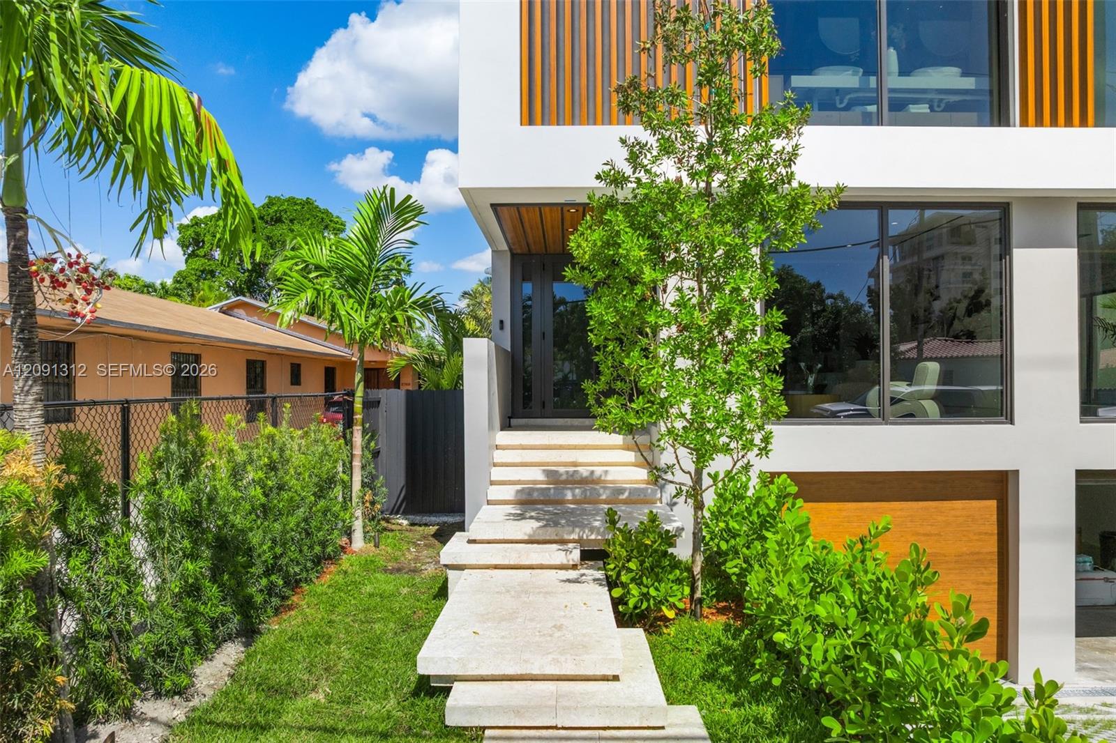 Modern architectural exterior featuring smooth white stucco finish, wood-slat cladding, expansive floor-to-ceiling glass windows, stone-paved floating staircase, and wood-paneled garage door