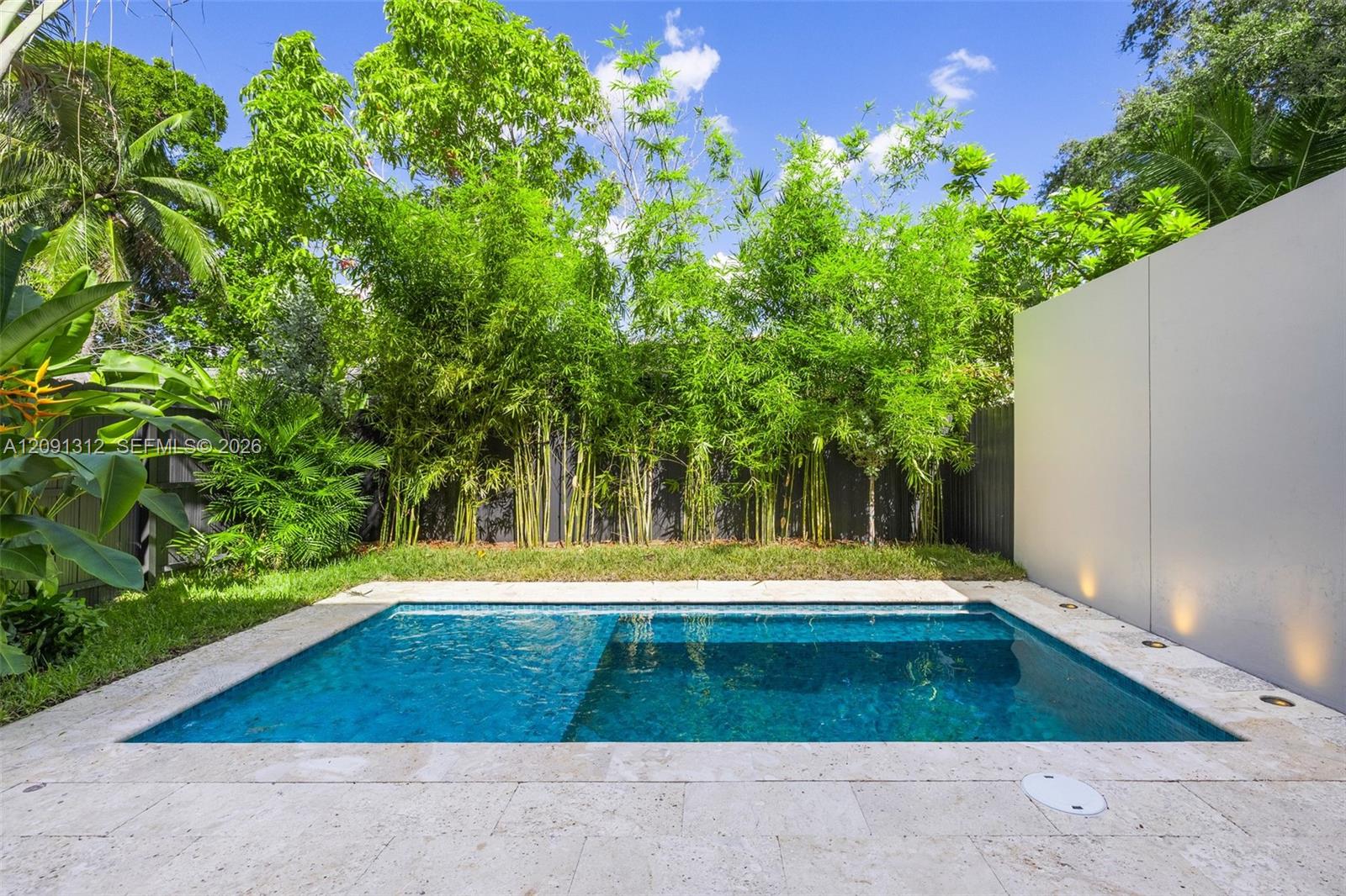 Swimming pool with natural stone decking, perimeter landscape screening, and integrated wall lighting