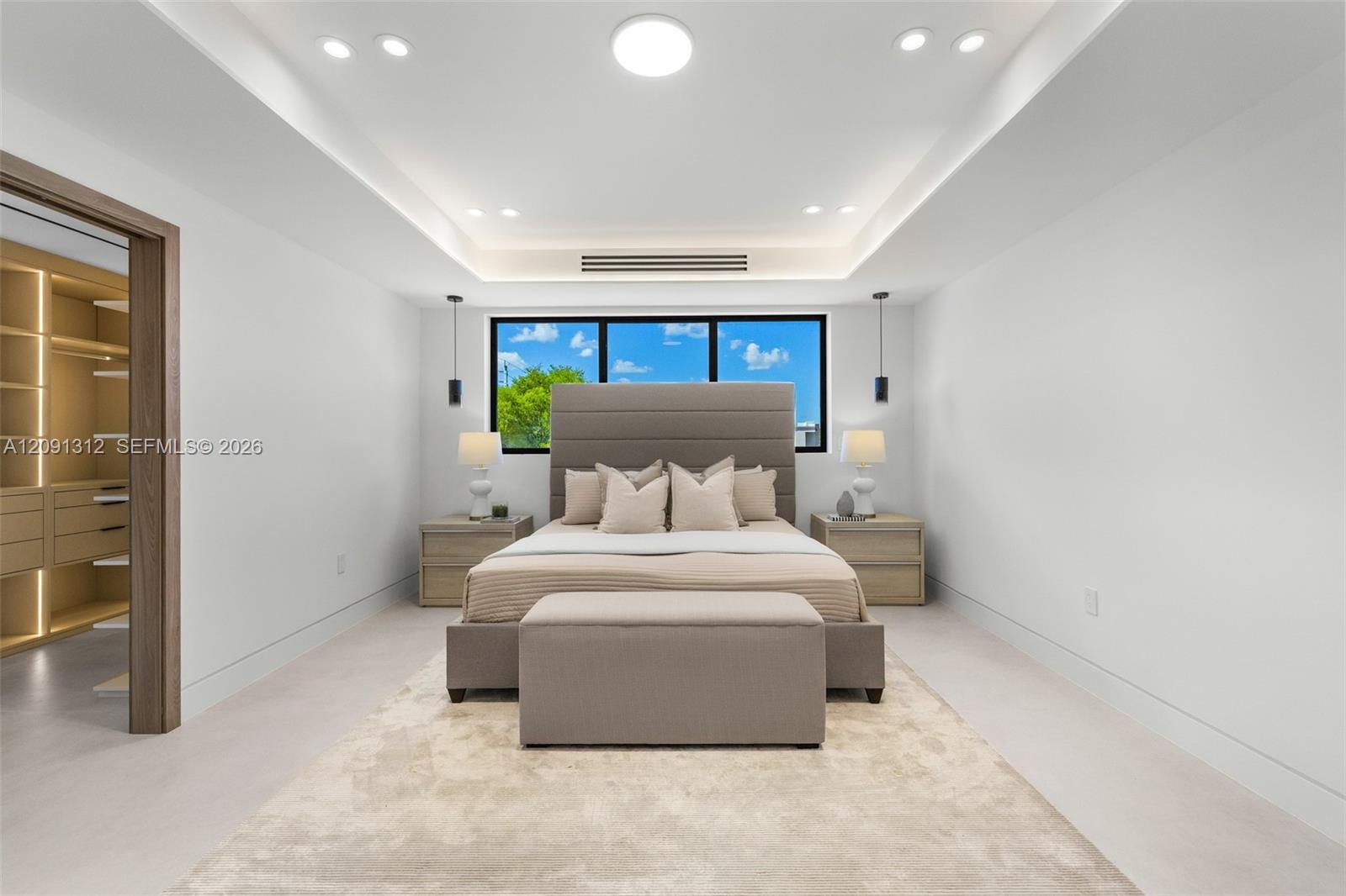 Tray ceiling with recessed lighting, integrated accent lighting, large windows with black frames, and a walk-in closet with built-in storage shelving
