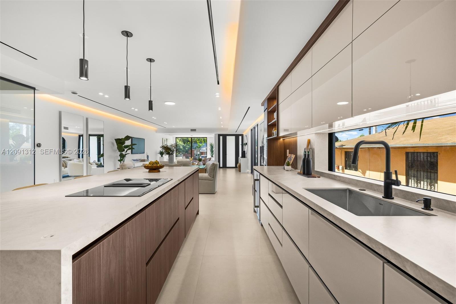 Modern kitchen featuring a spacious island with a built-in cooktop, high-gloss cabinetry, stone-finish countertops, matte black plumbing fixtures, and recessed accent lighting