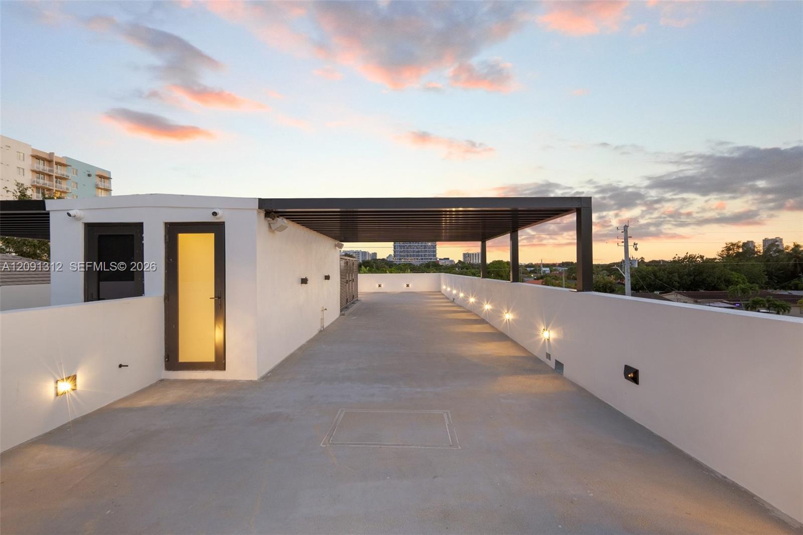 Rooftop terrace featuring smooth concrete flooring, solid perimeter walls, built-in wall-mounted lighting, and a metal-framed covered area