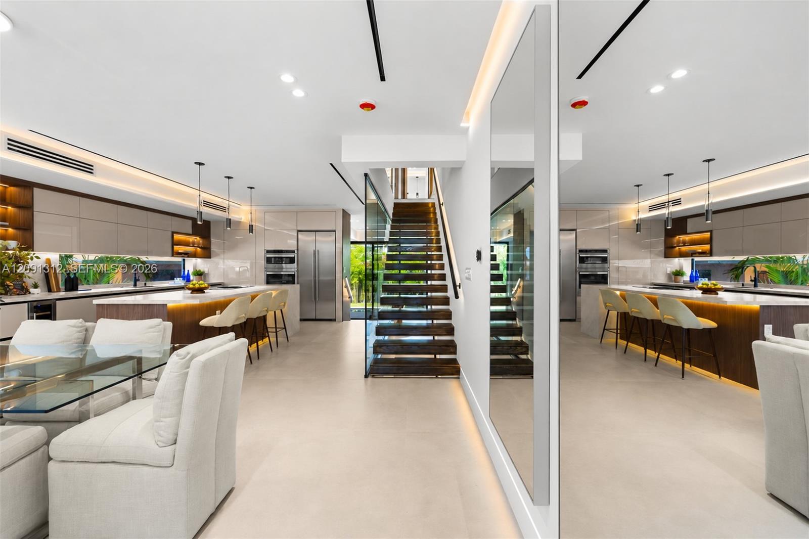 Modern open-concept area featuring sleek flat-panel cabinetry, a central island with integrated lighting, polished stone countertops, and a staircase with wood-tread risers and glass balustrades