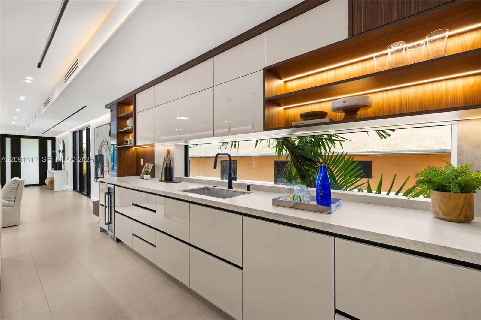 Sleek cabinetry with high-gloss finish, minimalist stone countertops, linear undermount stainless steel sink, matte black faucet, and recessed integrated shelving with accent lighting