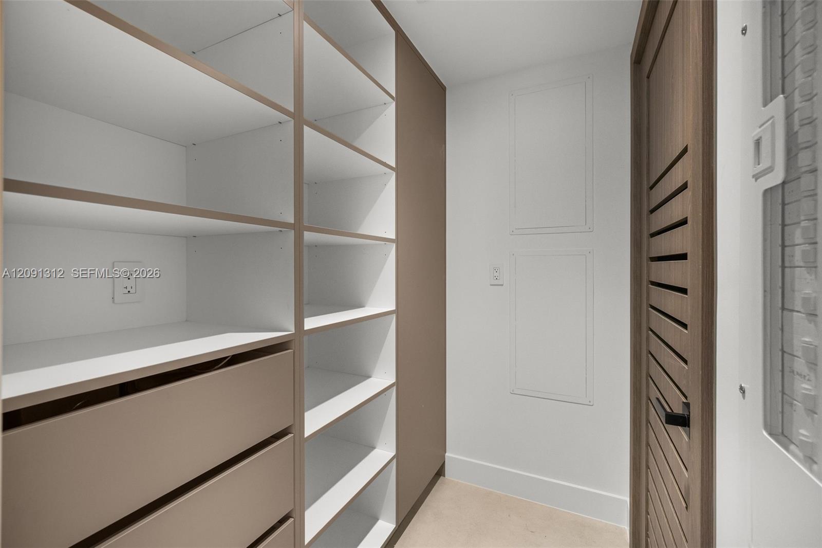 Custom built-in storage unit featuring adjustable shelving, integrated soft-close drawers, and a neutral wood-finish frame, complemented by a louvered-style door