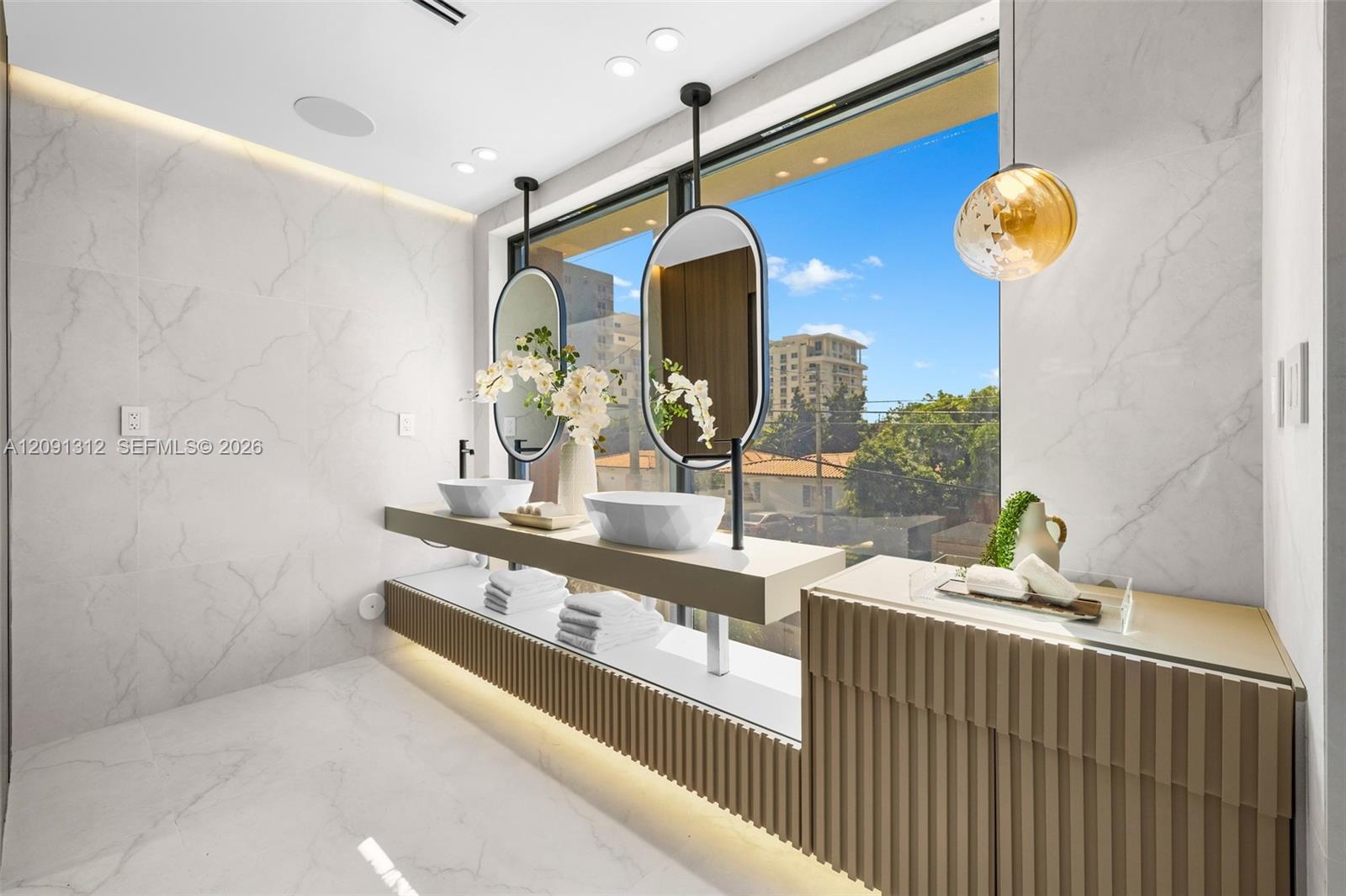 Floating dual-sink vanity with matte black hardware, integrated under-cabinet lighting, large-format tiled walls and flooring, and custom fluted cabinetry
