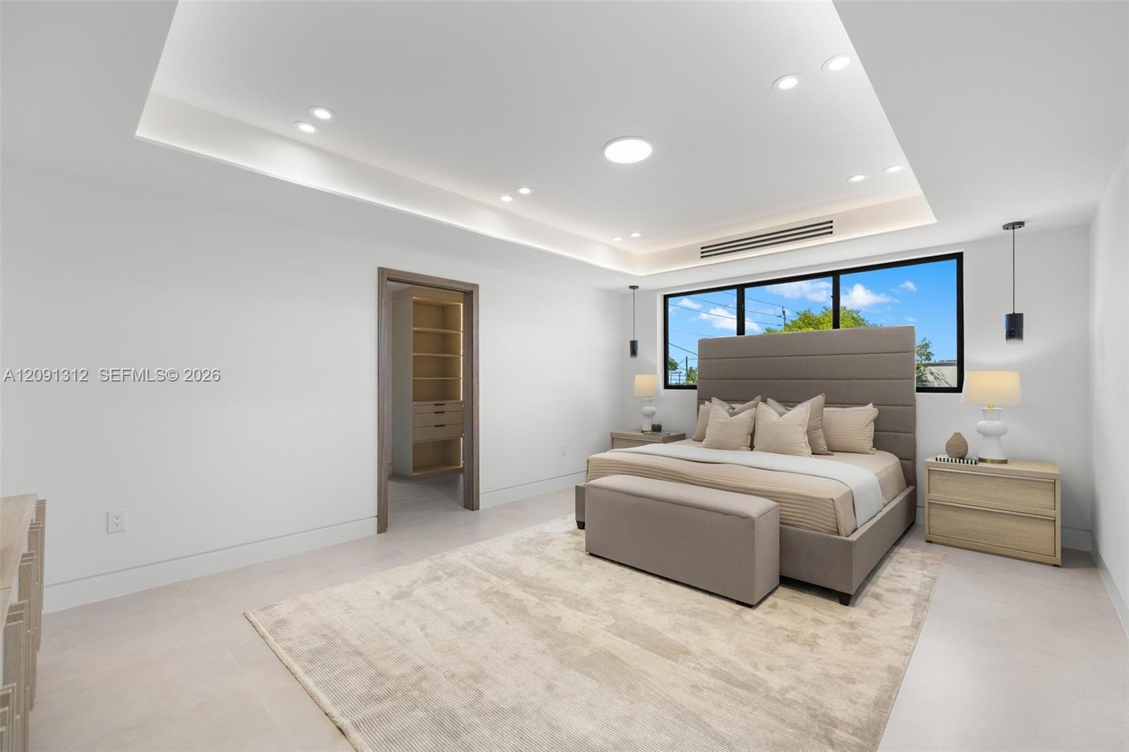 Tray ceiling with recessed ambient lighting, large-format tile flooring, oversized black-frame window, and built-in walk-in closet shelving