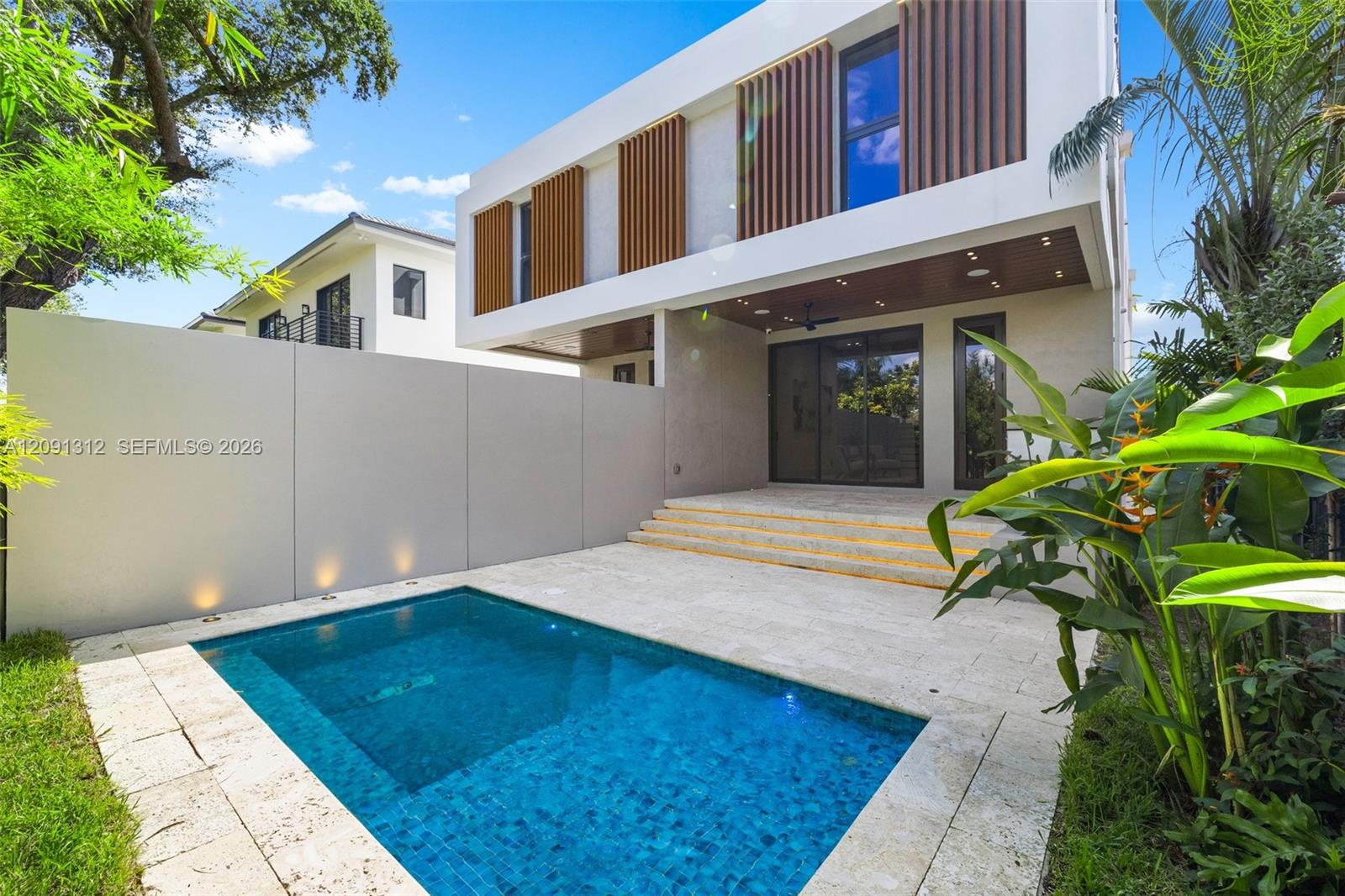 Modern two-story exterior with vertical wood-slat accents, featuring a stone-paved patio, an inground pool, tiered concrete steps, and integrated perimeter lighting