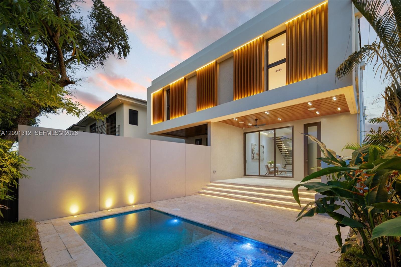 Modern architectural exterior featuring vertical wood-slat detailing, recessed integrated lighting, a stone-surround swimming pool, and a raised concrete patio with tiered steps