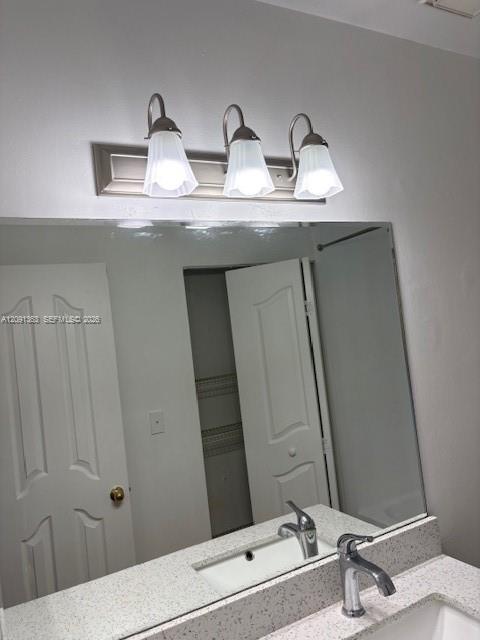 Large wall-mounted mirror above a vanity with stone-flecked countertop, undermount sink, metallic faucet, and a three-light fixture with fluted glass shades
