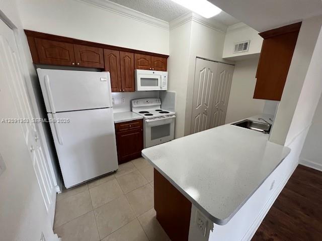 Kitchen featuring wood cabinetry, white appliances, solid surface countertops, and tile flooring