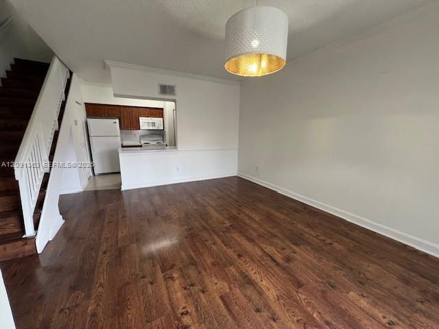 Wood-finish flooring, staircase with white railing, kitchen with dark wood cabinetry, white kitchen appliances, and textured drum pendant light fixture