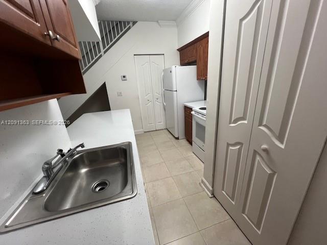 Kitchen featuring stone-finish countertops, stainless steel sink with metal faucet, wood-toned cabinetry, tile flooring, and bi-fold closet doors