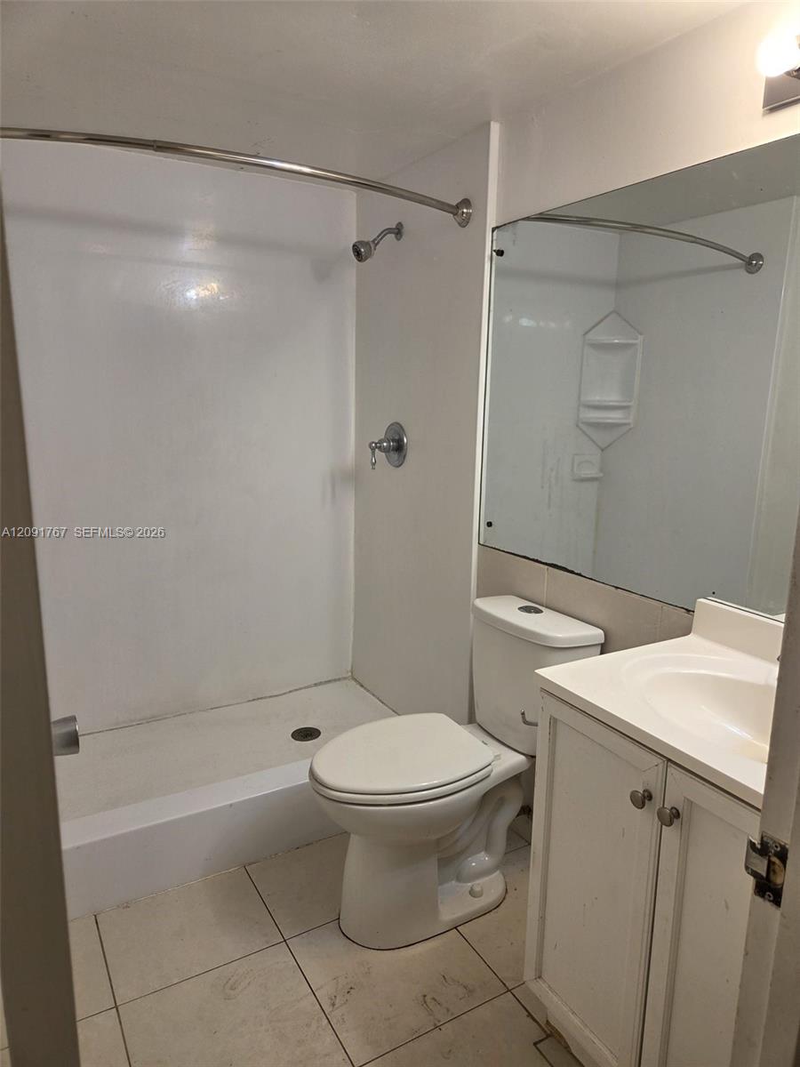 Bathroom featuring a walk-in shower with integrated shelving, white cabinetry, a single-basin vanity, and large-format tile flooring Bathroom featuring a walk-in shower with integrated shelving, white cabinetry, a single-basin vanity, and large-format tile flooring